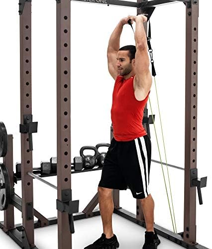 A muscular man in a red tank top performing a cable lat pulldown attached to the top of the Steelbody Monster Cage, with kettlebells and weight plates stored on the right plate horns